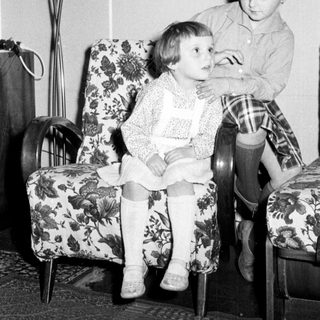 Here's a brief summary of the image: Two young girls seated in floral armchairs.