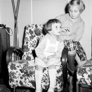 Here's a brief summary of the image: Two young girls seated in floral armchairs.