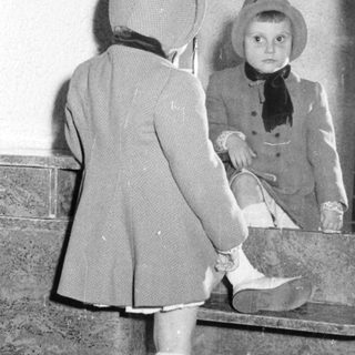 Child in a coat and hat looks in a mirror.