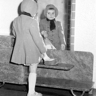 Child in a coat and hat looks in a mirror.