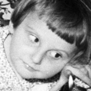 Child sits near a birthday cake with many candles.