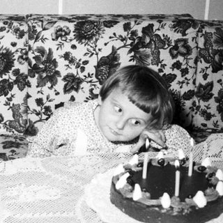 Child sits near a birthday cake with many candles.