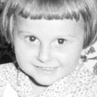Here's a brief summary of the image: Child sits in a patterned armchair, smiling for the camera.