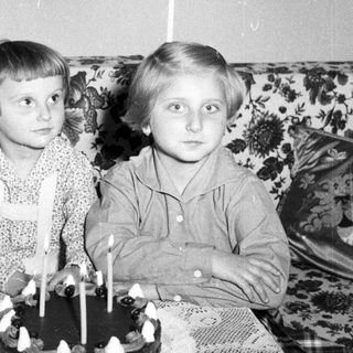 Two children with a birthday cake in a vintage setting.