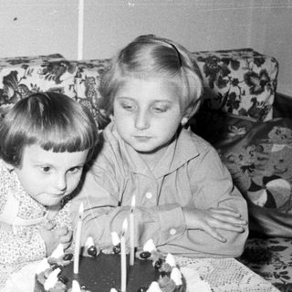 Two children sit near a cake with candles.