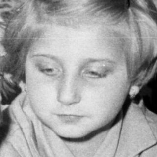 Two children sit near a cake with candles.