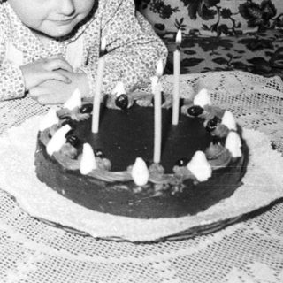 Child sits near a cake with candles indoors.