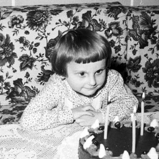 Child sits near a cake with candles indoors.