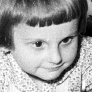 Child sits near a cake with candles indoors.