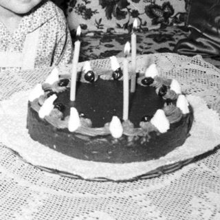 Child sits near a cake with lit candles.