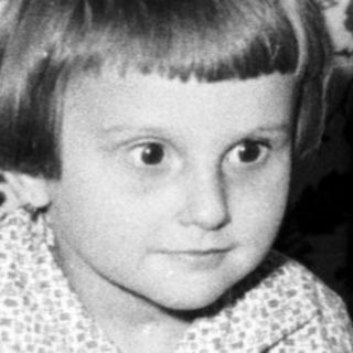 Child sits near a cake with lit candles.