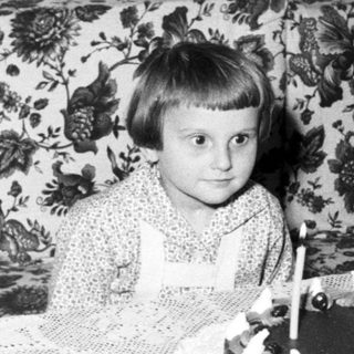 Child sits near a cake with lit candles.