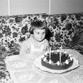 Child sits near a cake with lit candles.