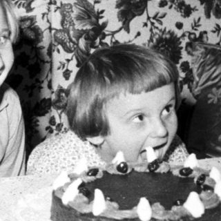 Here's a brief summary of the image: Two children celebrate with a cake and floral background.