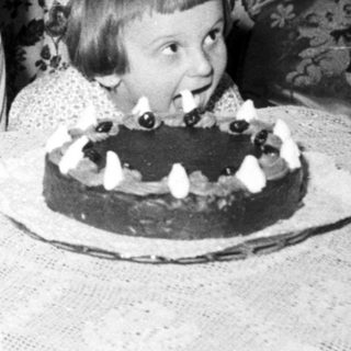 Here's a brief summary of the image: Two children celebrate with a cake and floral background.