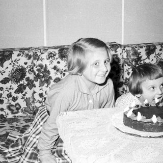 Here's a brief summary of the image: Two children celebrate with a cake and floral background.