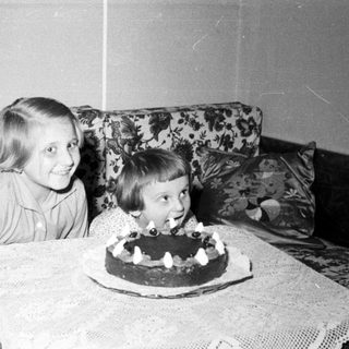 Here's a brief summary of the image: Two children celebrate with a cake and floral background.
