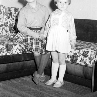 Two young girls sit beside a patterned couch.