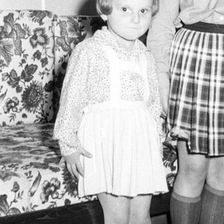 Two young girls pose formally in a vintage home interior.