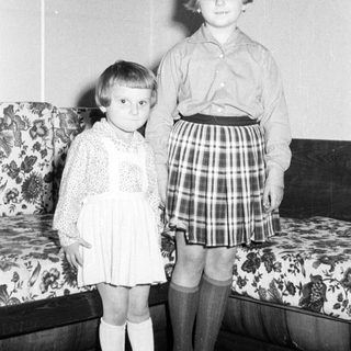 Two young girls pose formally in a vintage home interior.