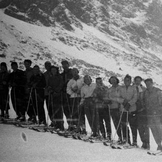 Group of people stand with skis in a snowy mountain setting.