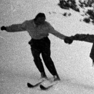 Three skiers descend a snow-covered slope in a vintage photo.