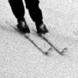 Three skiers descend a snow-covered slope in a vintage photo.