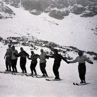 Group of people skiing and holding hands in snow.