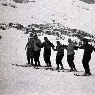 Group of people skiing and holding hands in snow.