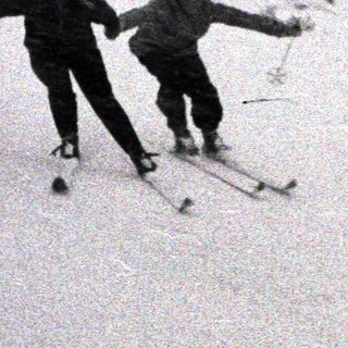 Two people ski down a snowy, mountainous slope.