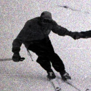 Two people ski down a snowy, mountainous slope.
