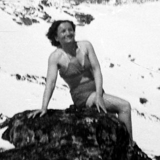 Woman sits on rock in snowy, mountainous landscape.