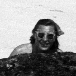 Man smiles among rocks and snow in a monochrome scene.