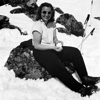 Here's a brief summary of the image: Woman sits on a rock in a snowy, mountainous landscape.