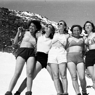 Five women in swimwear pose on a snowy mountainside.