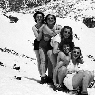 Group of people in swimwear pose on a snowy hillside.