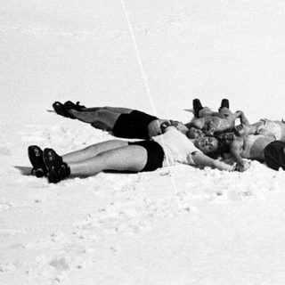 Here's a brief summary of the image: Three men lie prone in the snow, appearing injured.