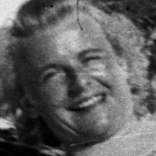 Woman in winter clothes lies in the snow, smiling.