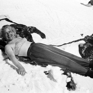 Woman in winter clothes lies in the snow, smiling.