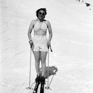 Here's a brief summary of the image: Woman in swimwear skis on a snowy slope.