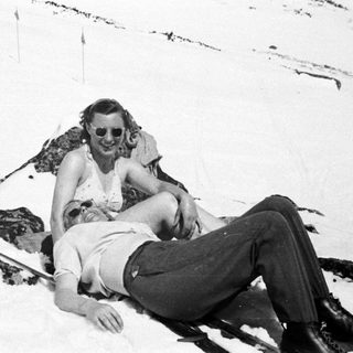 Couple relaxes in snow near skis and rocks.