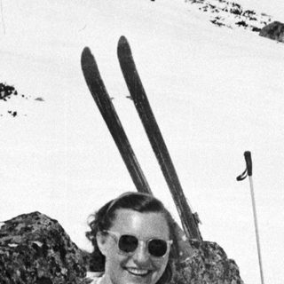 Woman in vintage swimsuit sits on snow with skis.