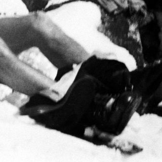 Man reclines in snow, wearing boots and shorts.