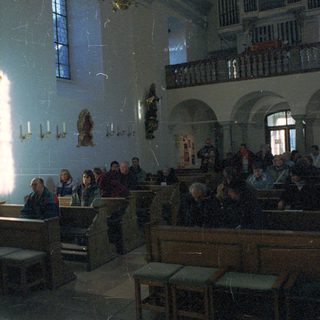 People seated in a church with statues and balconies.