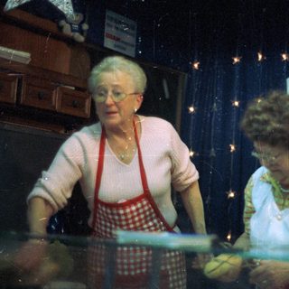 Two women work behind a display case, likely at a shop.