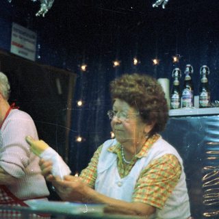 Two elderly women work behind a decorated counter.