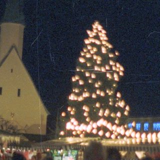 A brightly lit Christmas tree stands near a church.