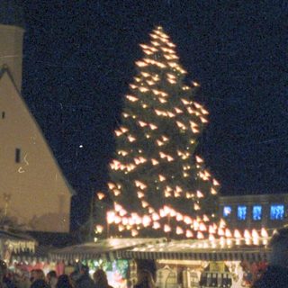 People stroll past a decorated tree and market stalls.