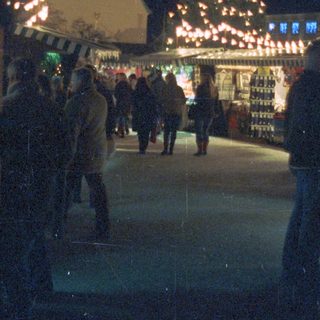 People stroll past a decorated tree and market stalls.