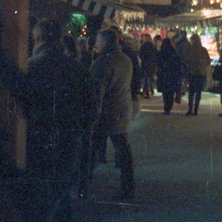 People stroll past a decorated tree and market stalls.